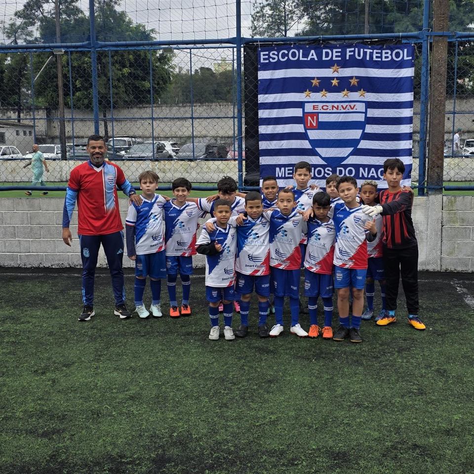 Turma do Nacional posada com o professor em frente à faixa da escola de futebol